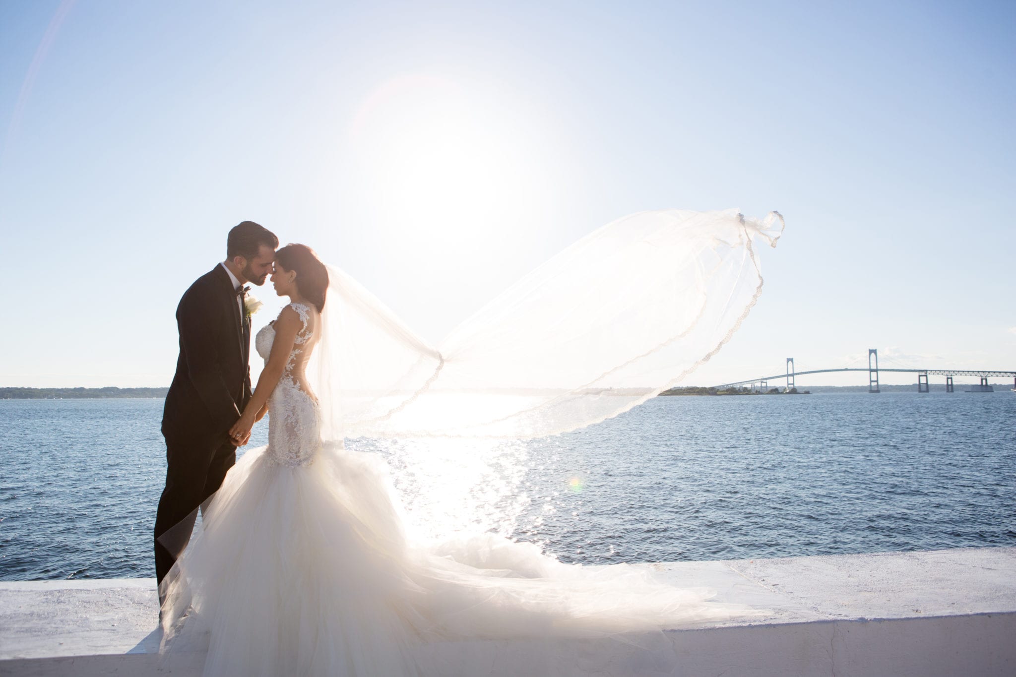 Bride and groom kissing by the sea with flowing veil during "I Do" moment