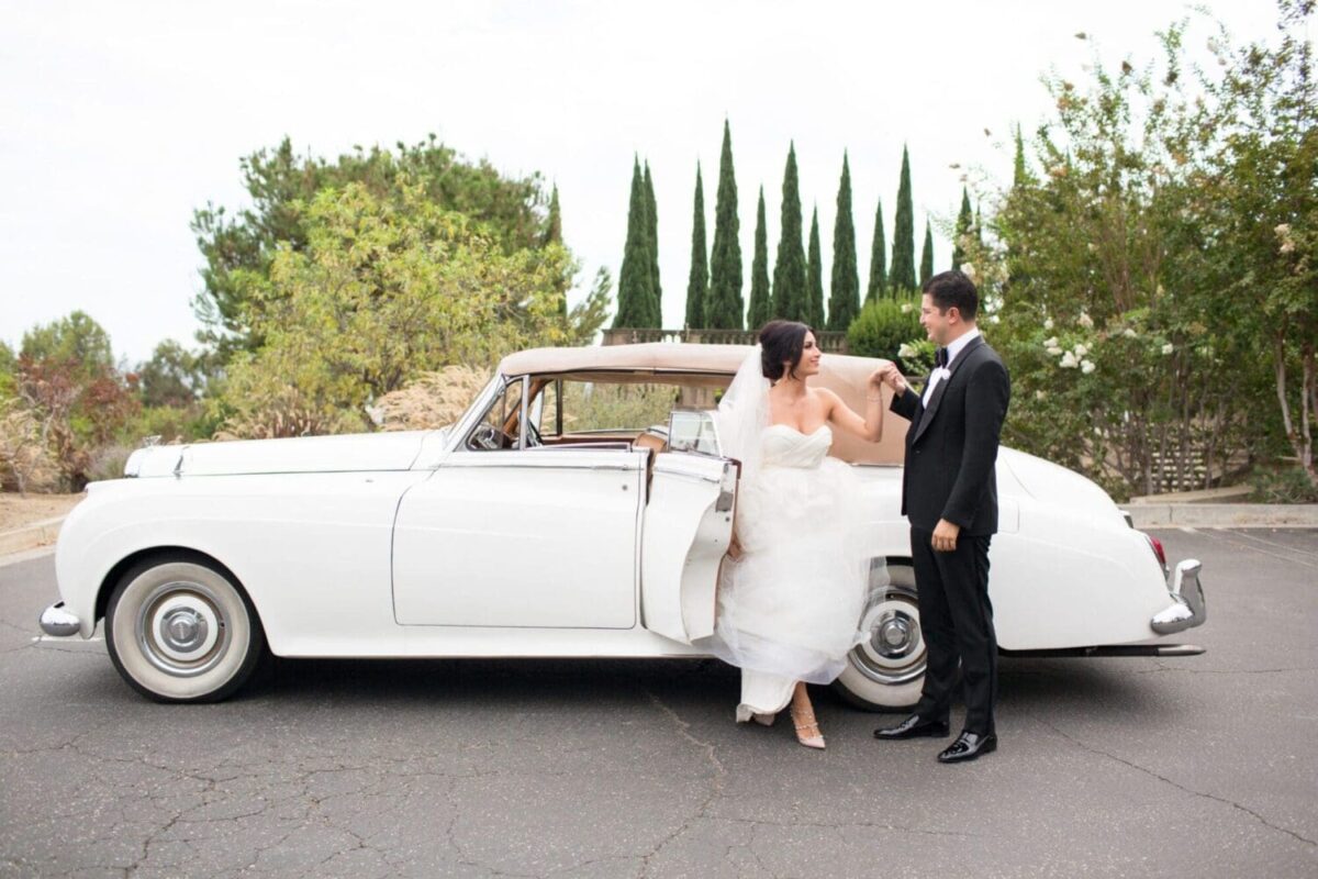 Bride and groom by a classic white car in a garden setting