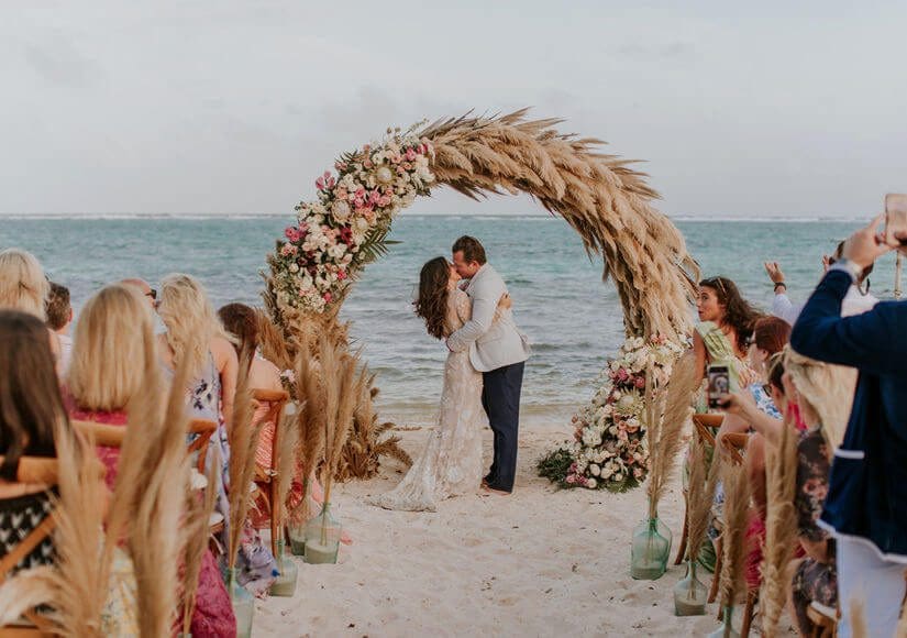 Couple kissing under floral arch at beach wedding in Mexico