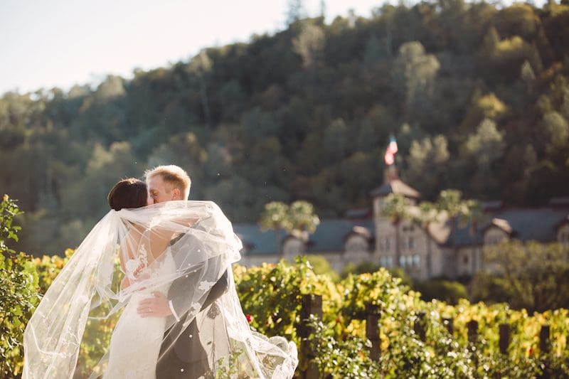 Bride and groom embracing in a vineyard, Napa Valley winery in background