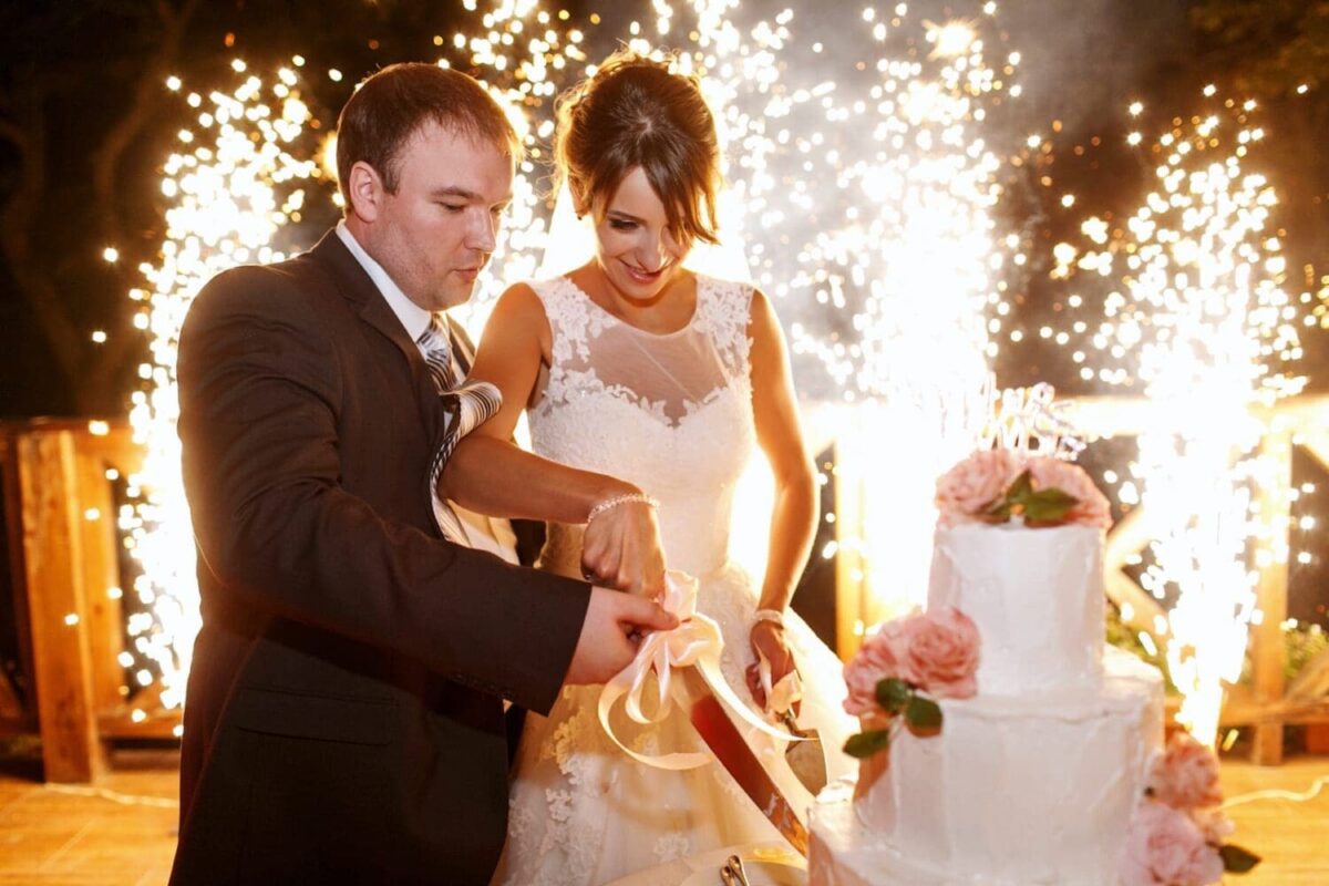 Bride and groom cutting wedding cake with fireworks in the background