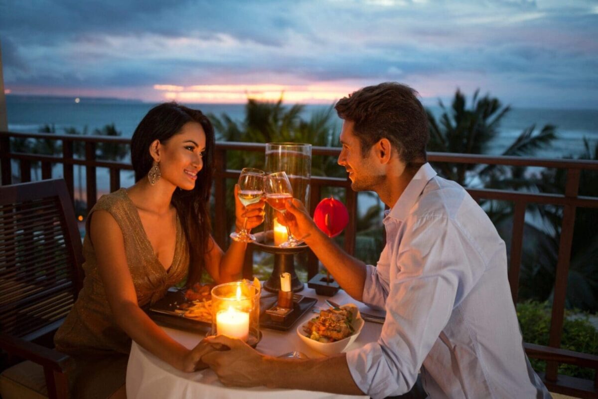 Couple toasting wine glasses at a candlelit dinner by the beach