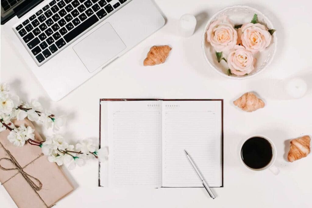 Open planner with laptop, flowers, and coffee on a desk, symbolizing wedding planning