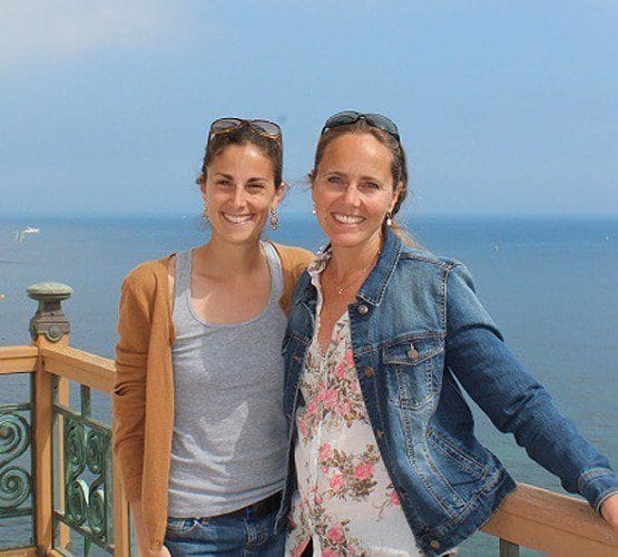 Two women smiling on a balcony overlooking the ocean, ideal inspiration for hiring a destination wedding planner.