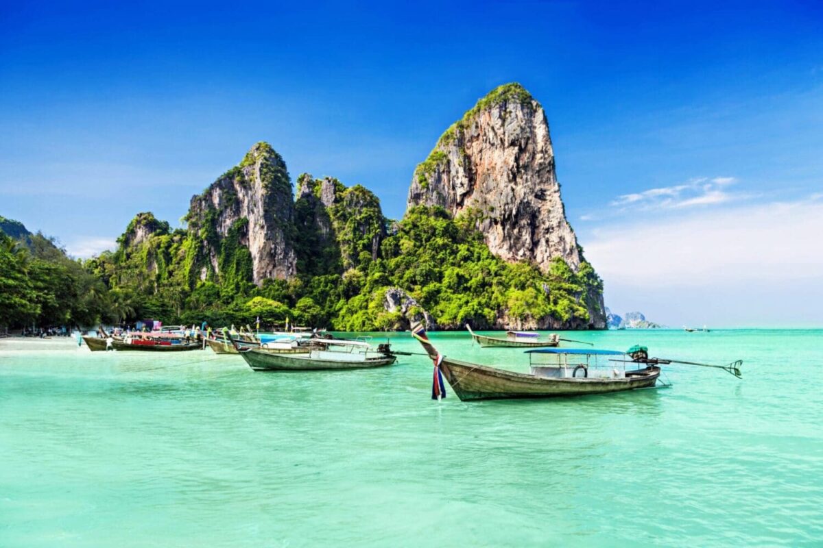 Longtail boats on turquoise water with limestone cliffs in Thailand
