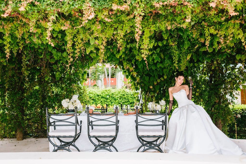 Bride in elegant gown beside a table under lush greenery at an all-inclusive resort