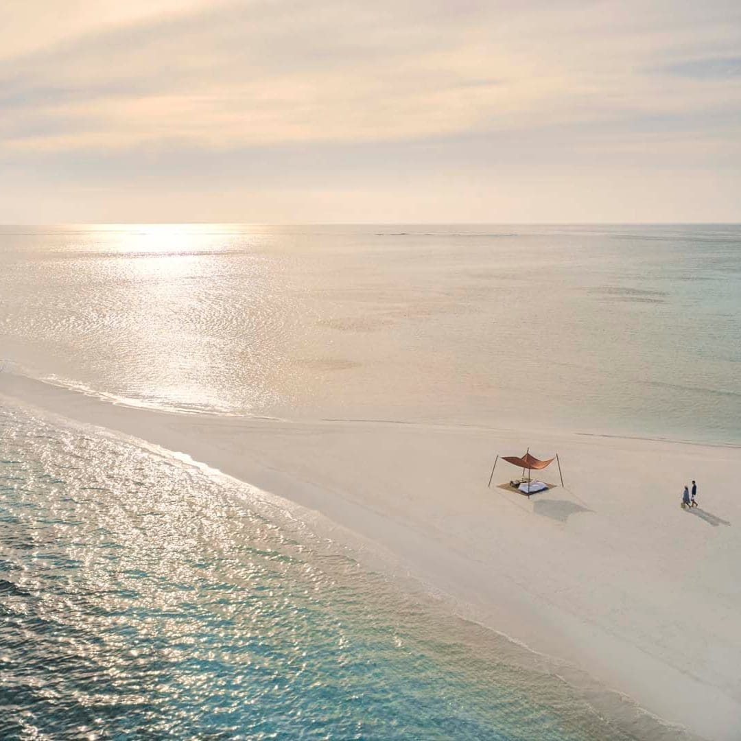 Beach honeymoon travel scene with a shaded canopy and turquoise water.