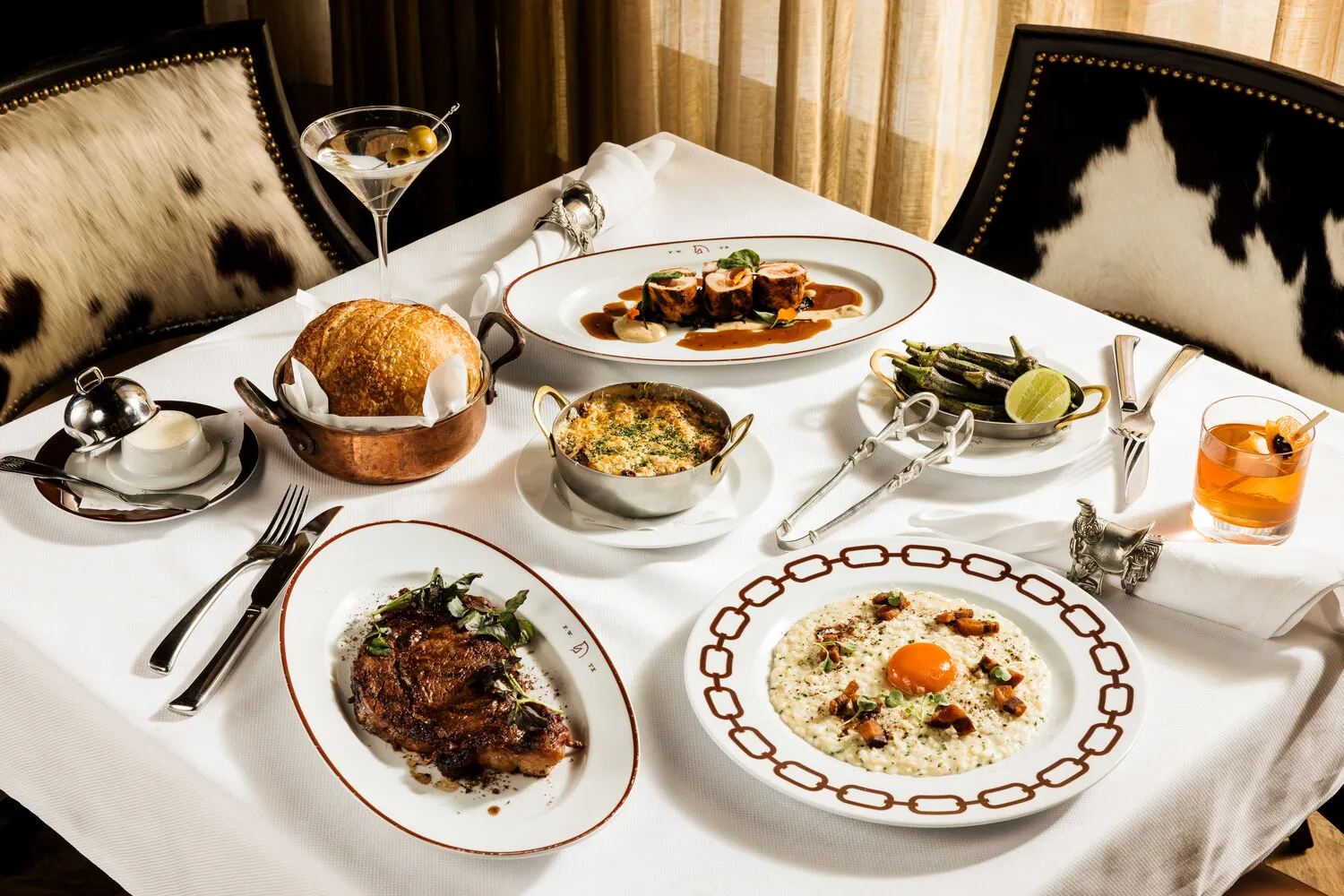 Elegant table setting with steak, risotto, and other dishes at Bowie House, Auberge Resorts Collection.