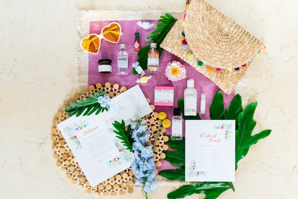 Flatlay of tropical-themed wedding welcome bags with mini bottles, sunglasses, and order of events. Perfect wedding gift bags.