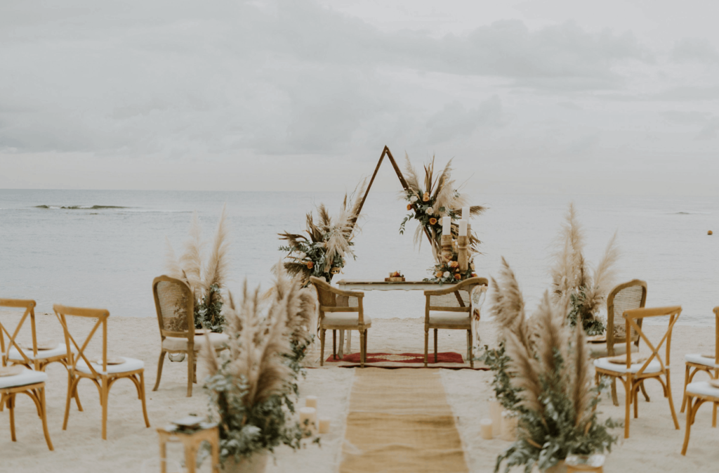 Beach wedding ceremony setup in Dominican Republic with pampas grass and wooden chairs.