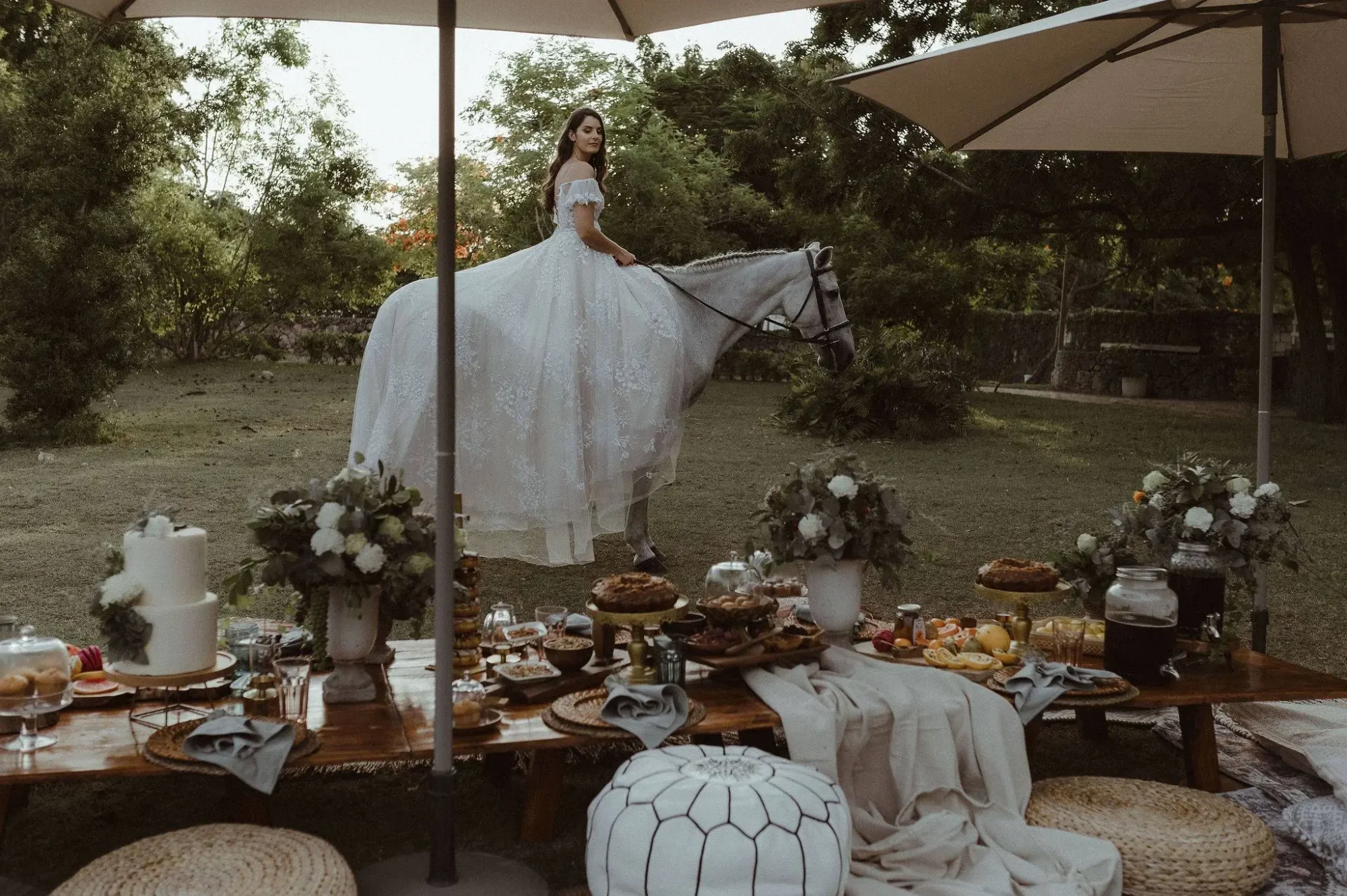Bride in flowing gown sits on a white horse at a romantic Dominican Republic wedding picnic.