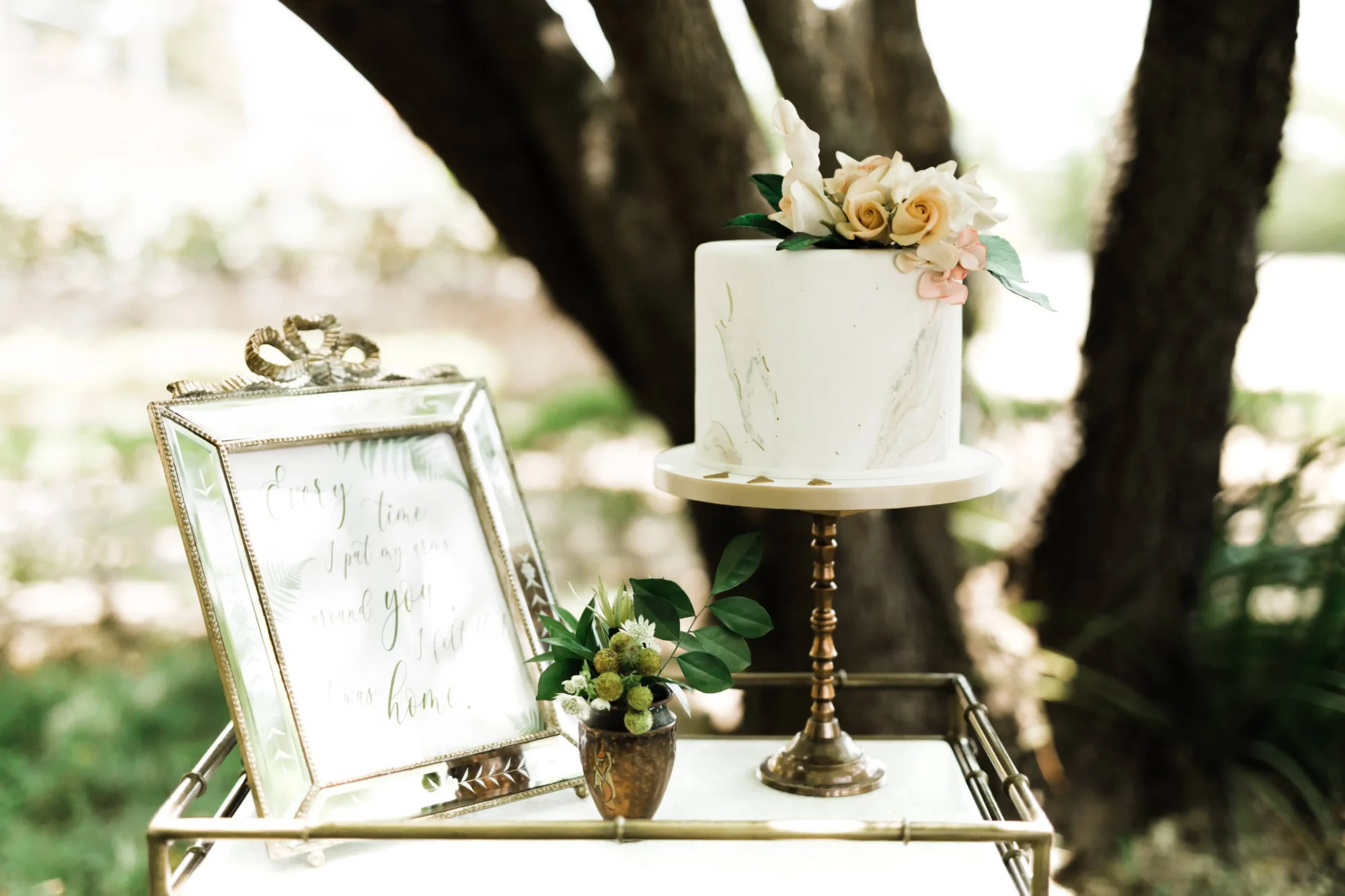 Elegant wedding cake with flowers, displayed on a gold stand, next to a framed quote. Perfect for a Dominican Republic wedding at Casa Hemingway.