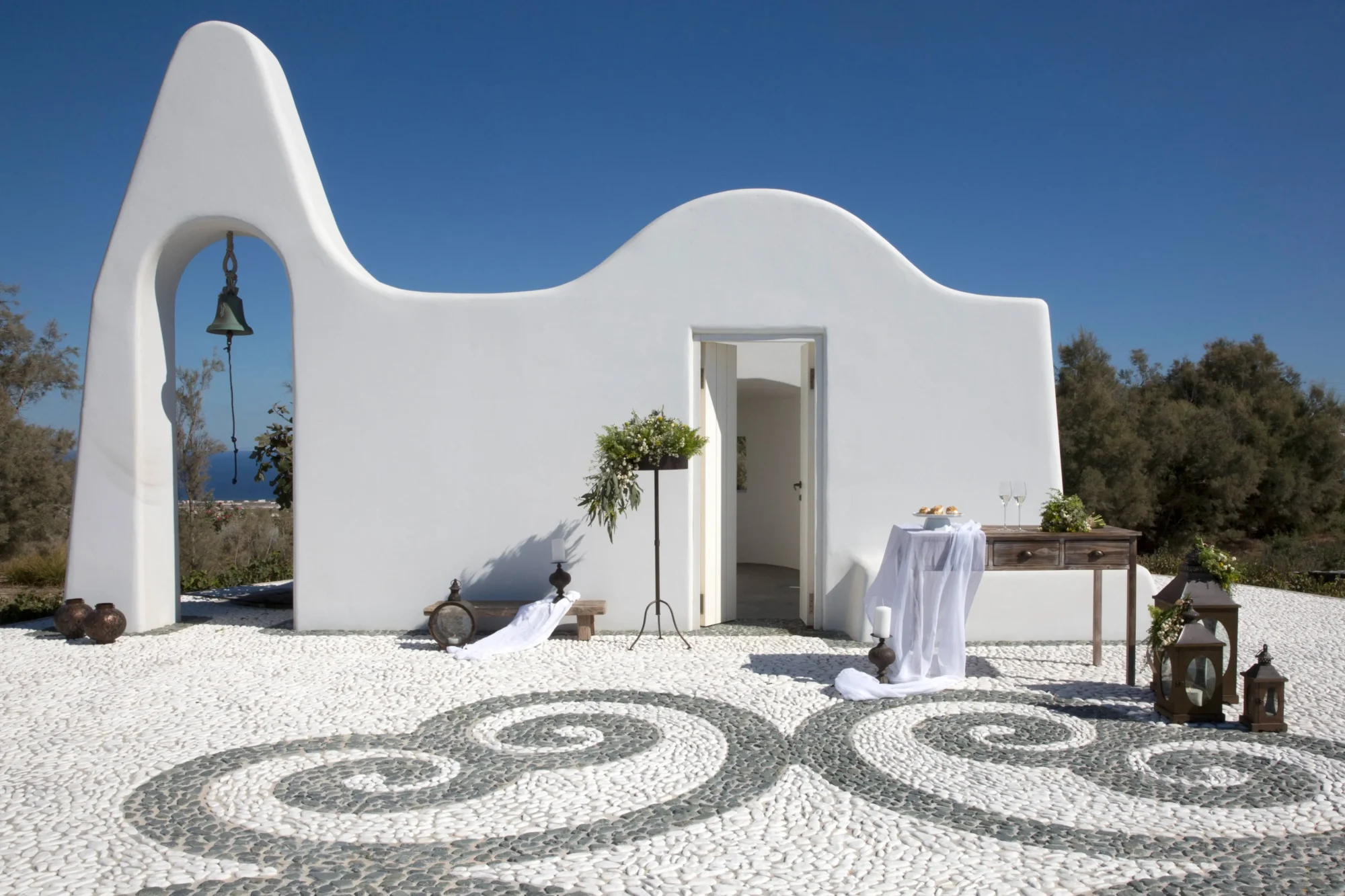 Santorini dream wedding ceremony setup: whitewashed chapel, pebble pathway, floral arrangements.