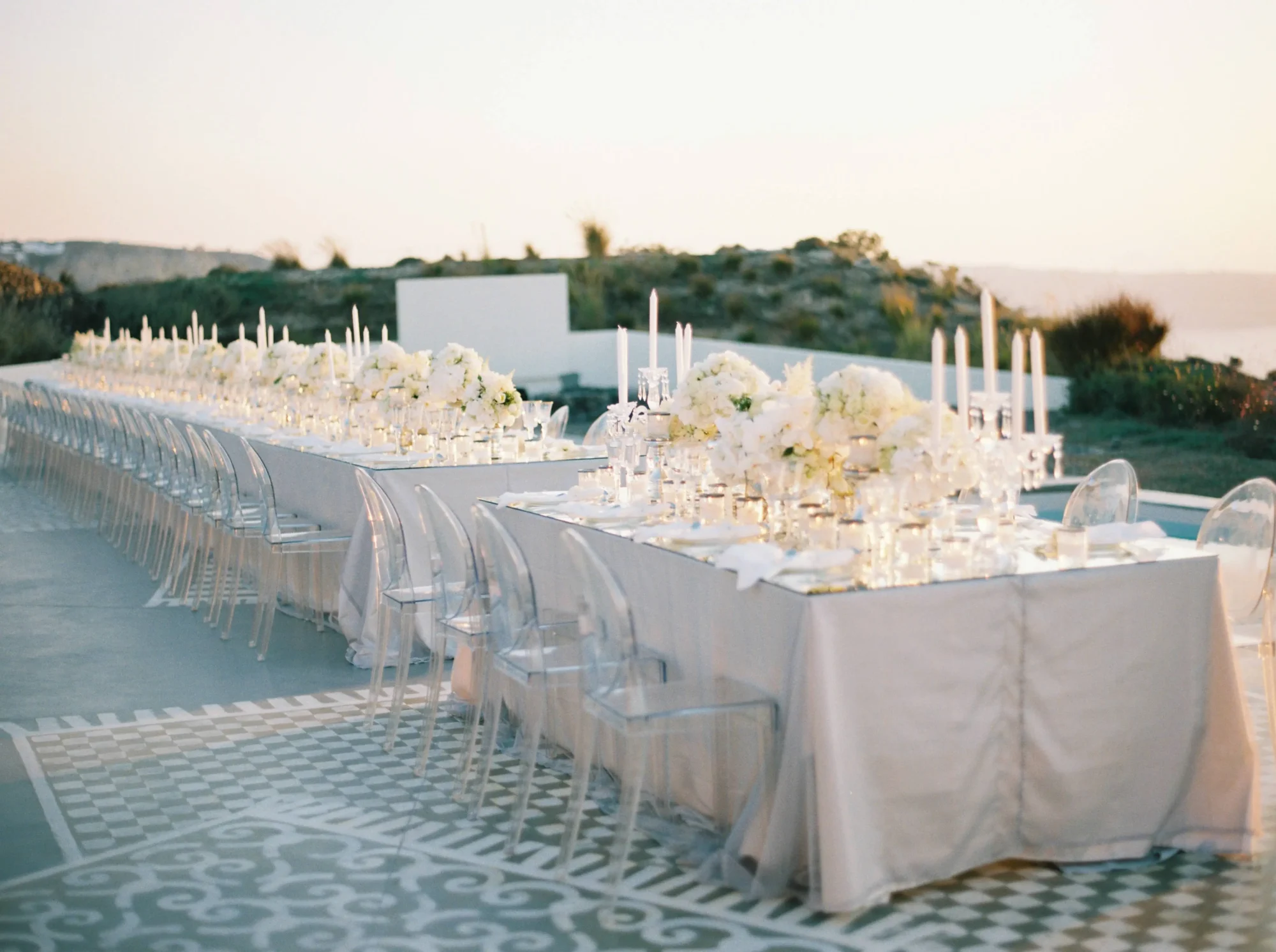 Elegant long wedding reception tables in Santorini, decorated with white flowers and candles. Dream wedding setting.