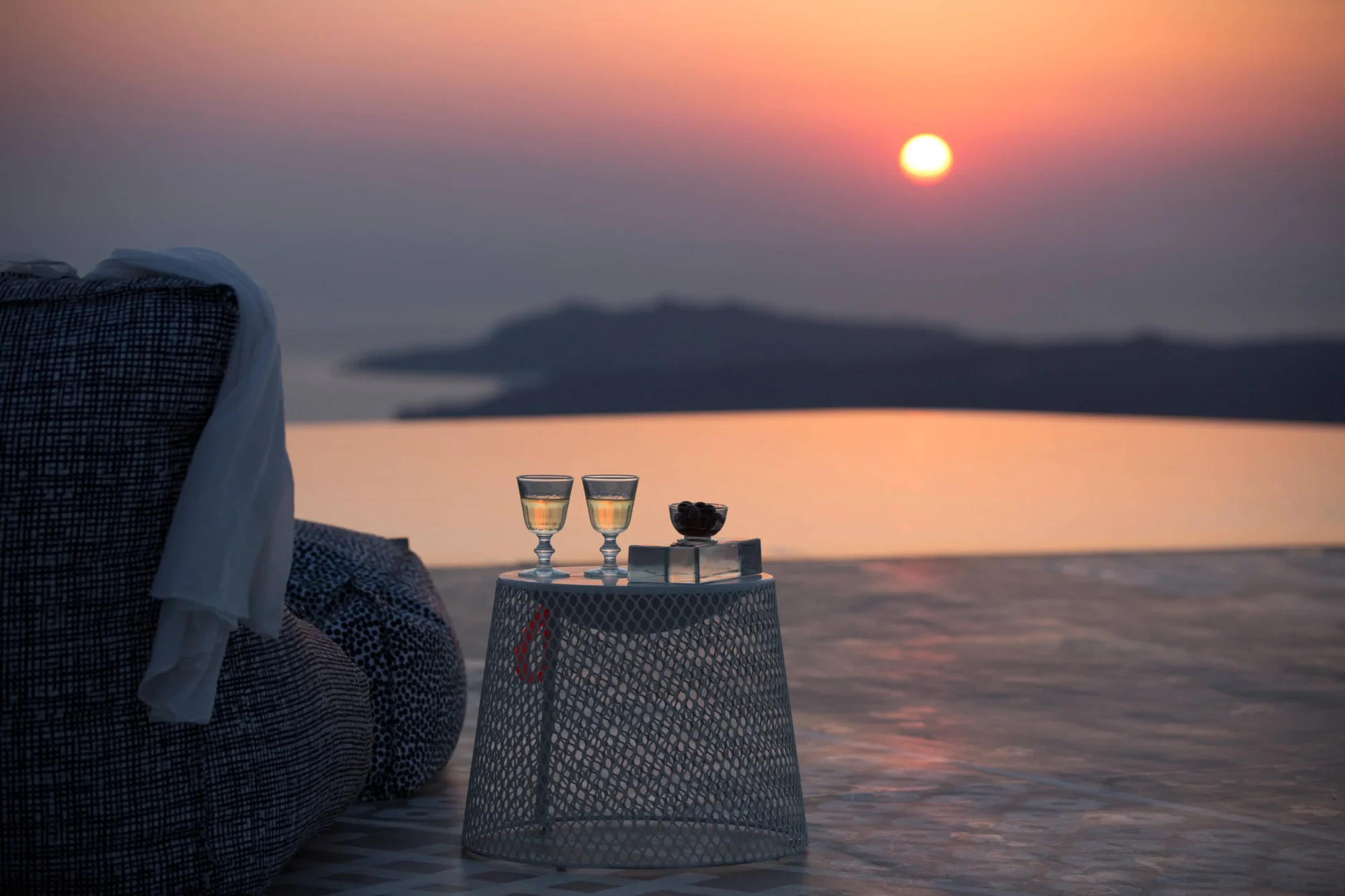 Romantic Santorini sunset: two glasses of wine on a table overlooking the Aegean Sea. Dream wedding in Santorini.