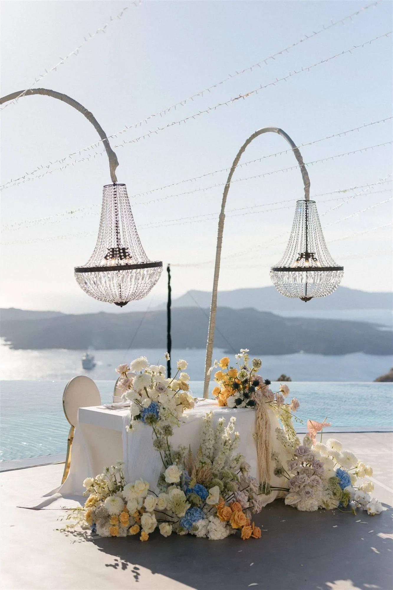 Romantic Santorini wedding ceremony setup with floral arrangements and crystal chandeliers.