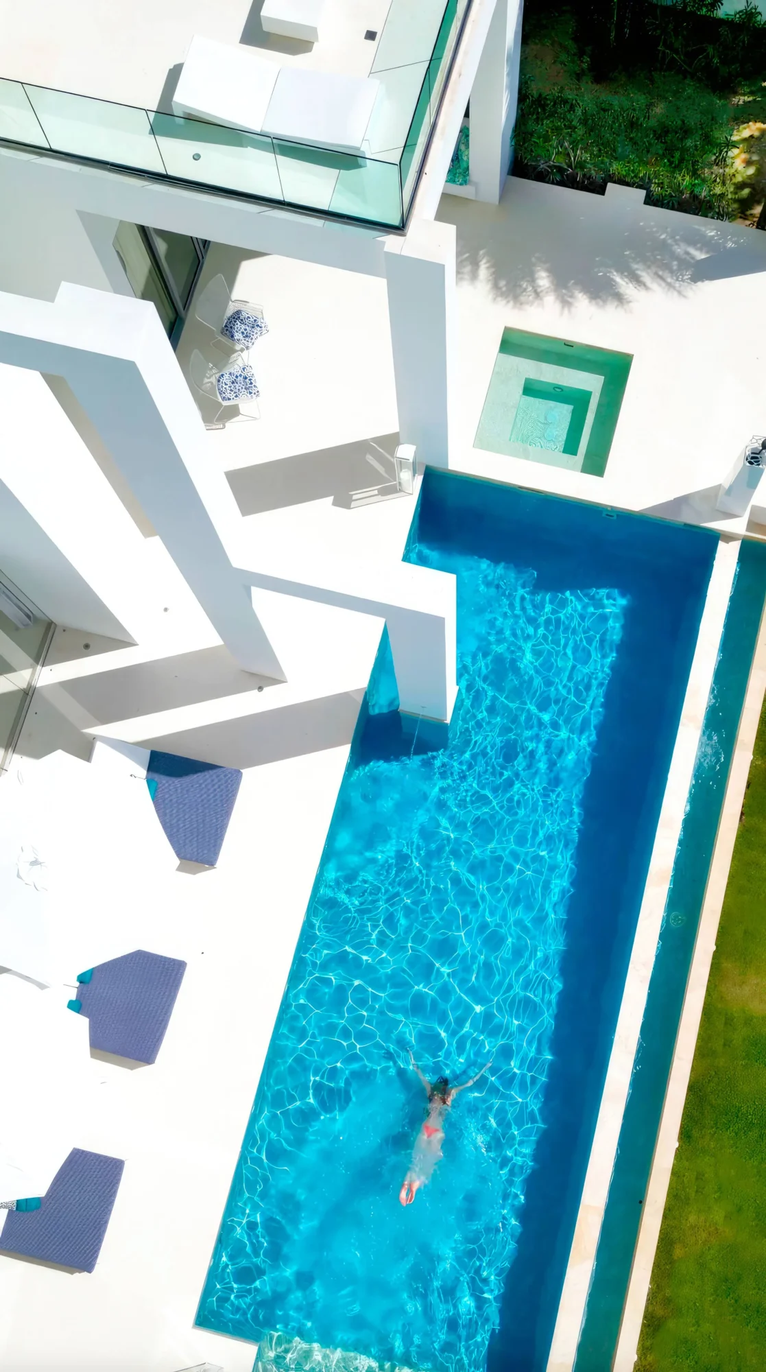 Aerial view of a woman swimming in a luxurious infinity pool at a modern white beach house. Perfect Anguilla destination wedding location.