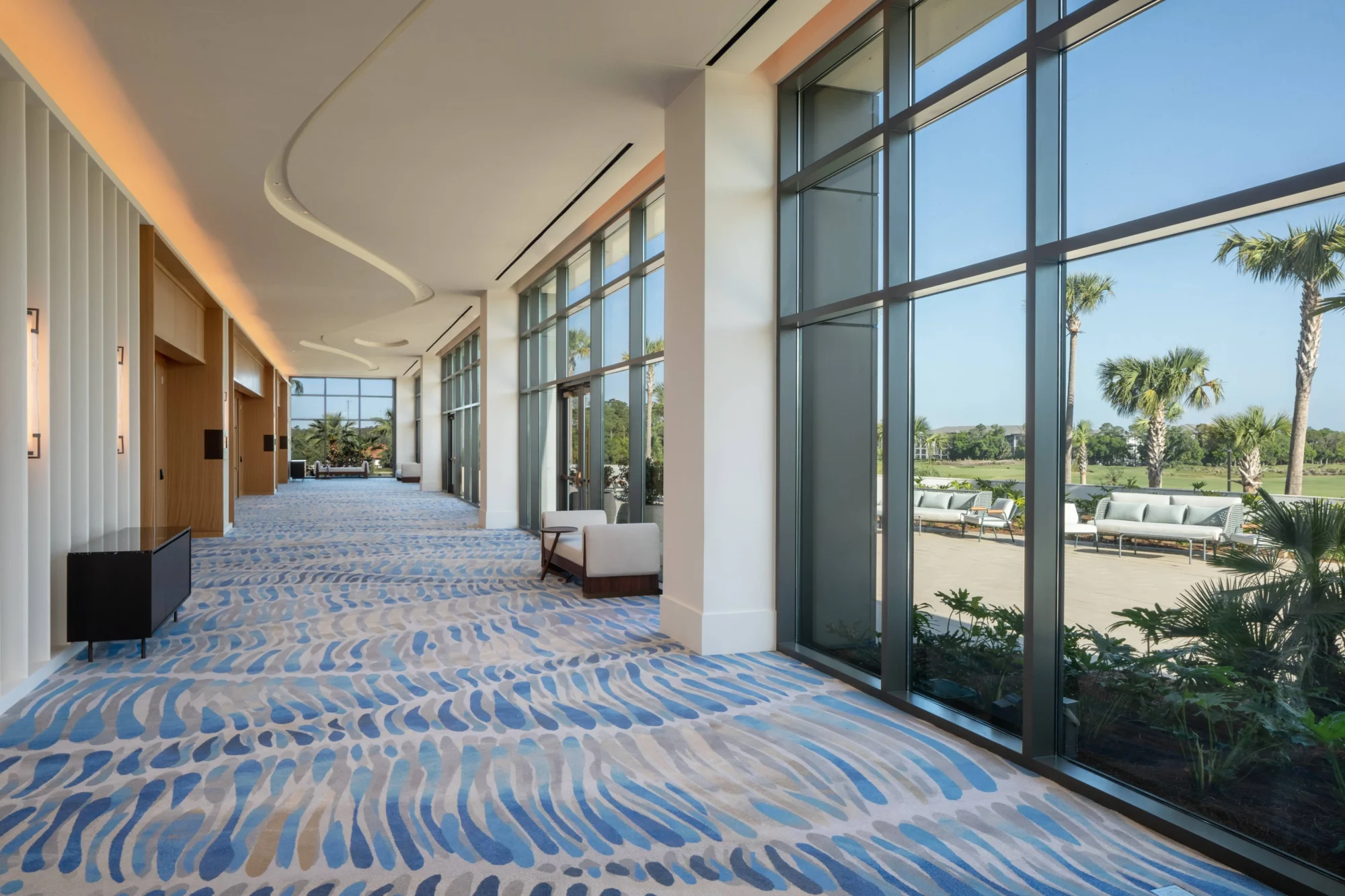 Hallway with large windows overlooking a patio and palm trees at the Conrad Orlando wedding destination.