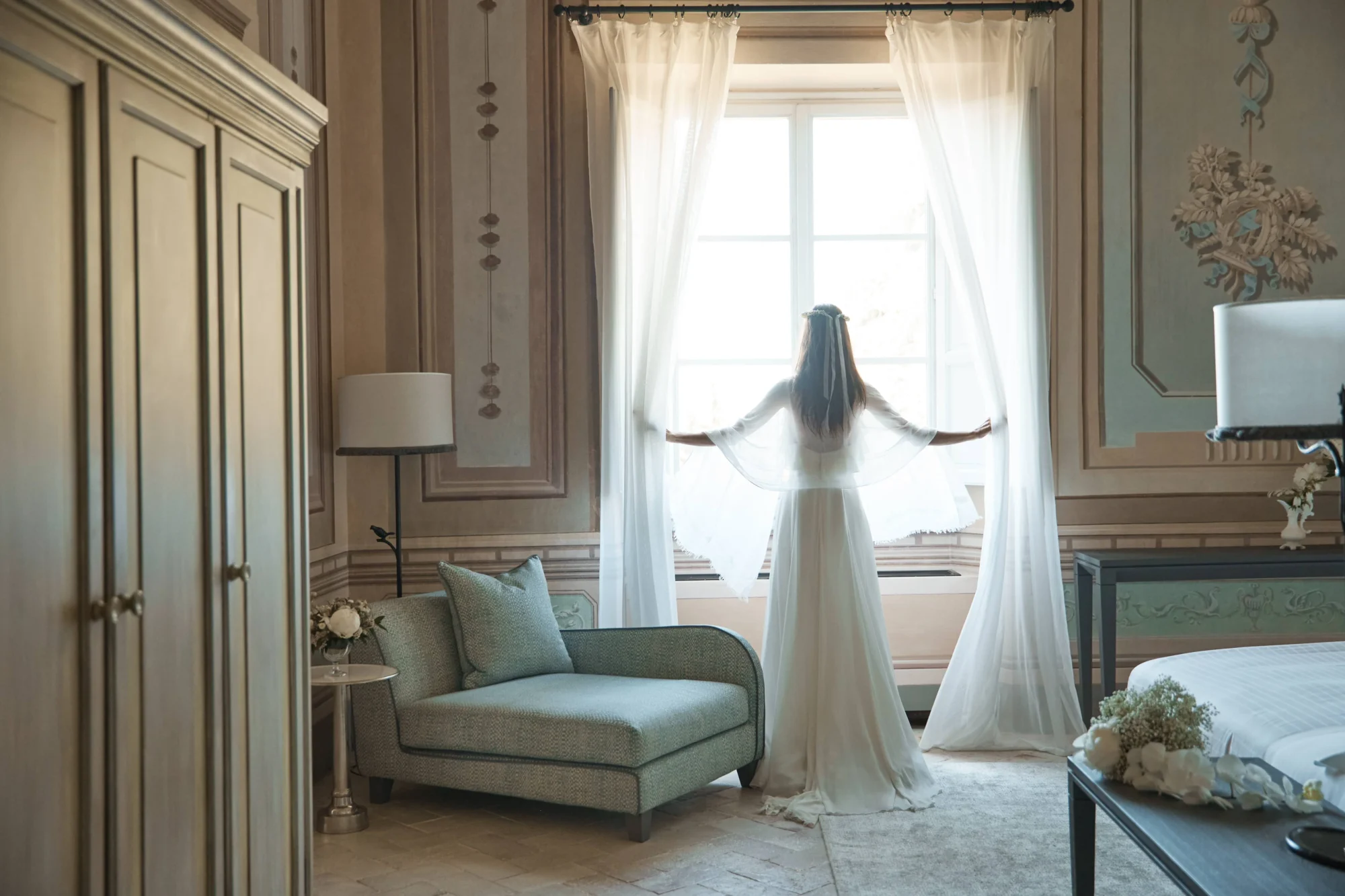Bride in wedding dress at a Tuscany Castle wedding, looking out a window at COMO Castello Del Nero.