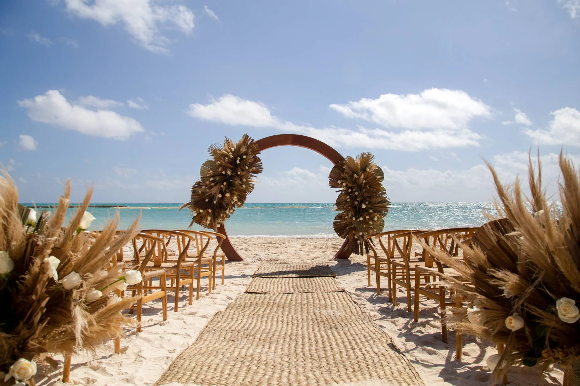 Beach wedding ceremony setup at Fairmont Mayakoba in Riviera Maya with arch and chairs.