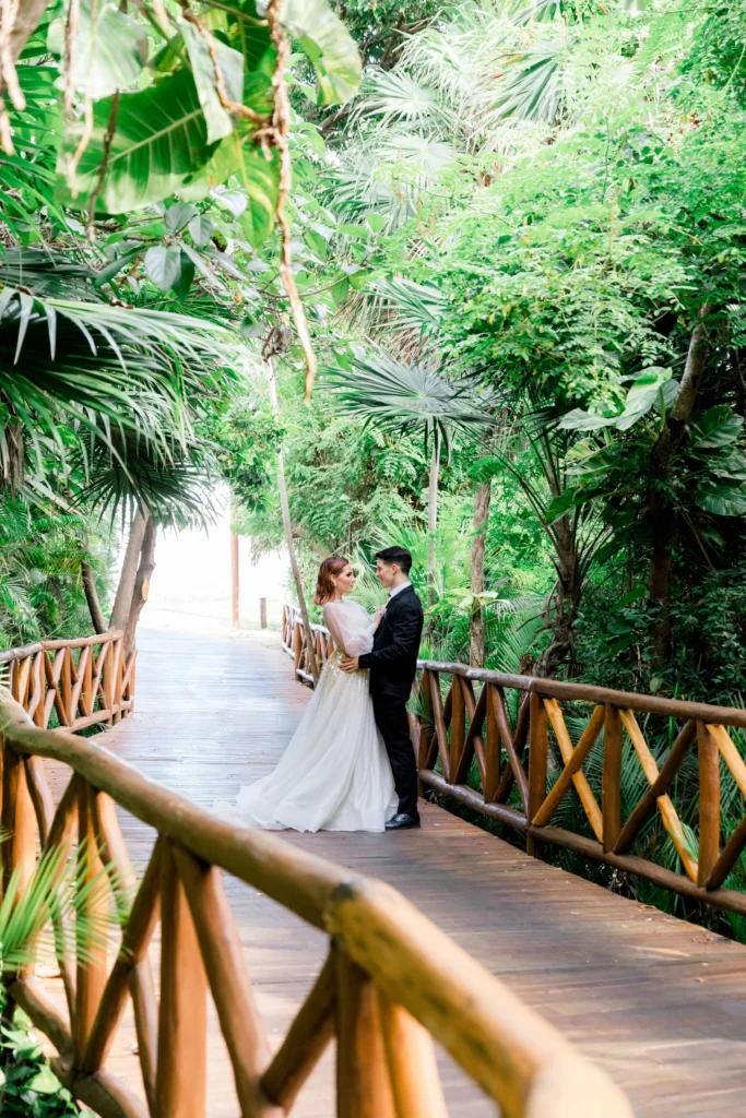 Bride and groom embrace on a wooden bridge in a Riviera Maya beach wedding setting.