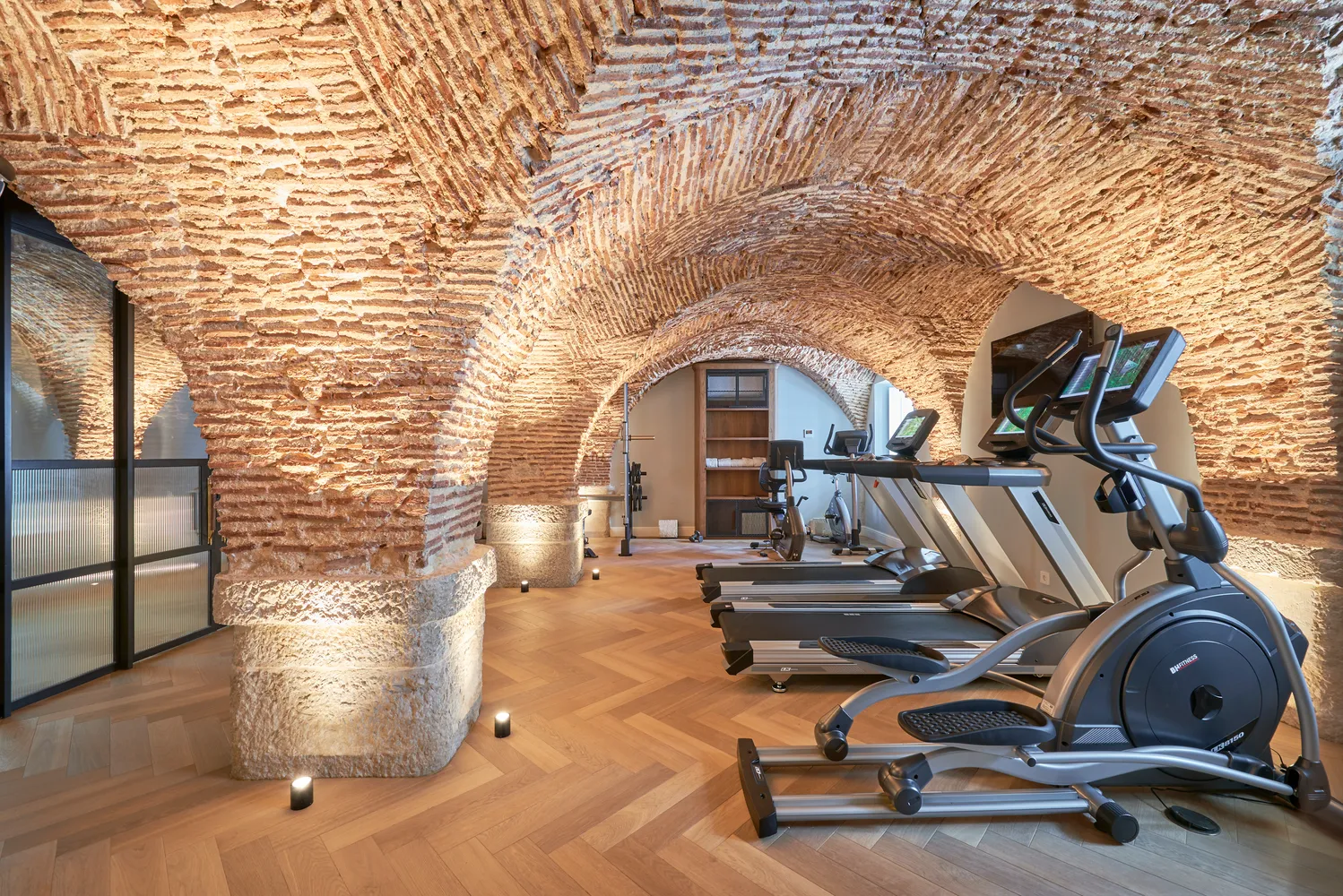 Modern gym at Palácio Ludovice Hotel, featuring treadmills and elliptical machines in a historic brick-vaulted room.