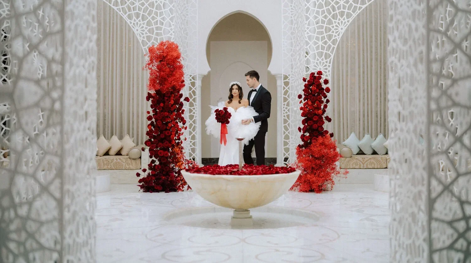 Bride and groom pose for a wedding photo at the Royal Mansour Marrakech. Red floral arrangements decorate the luxurious setting.