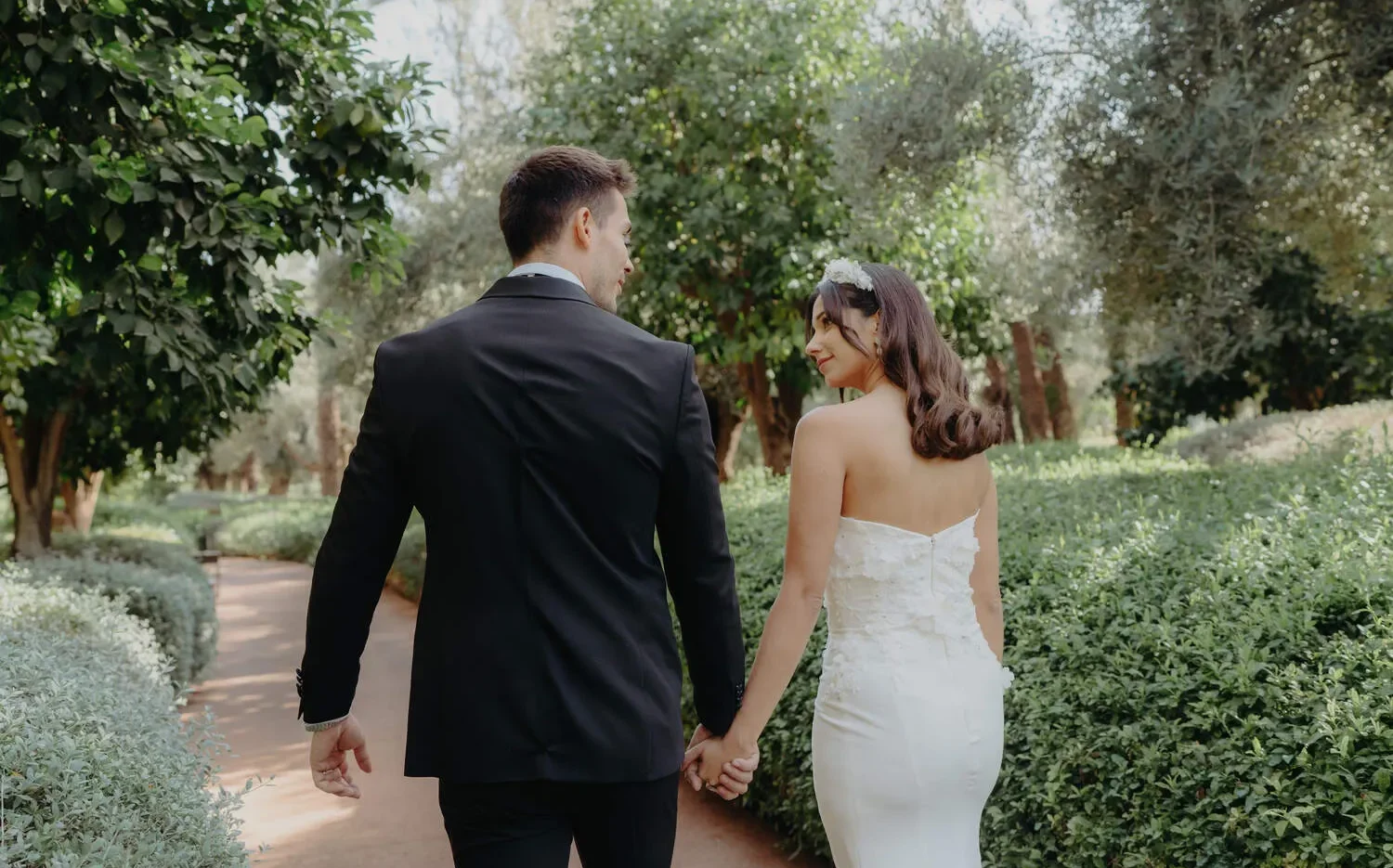 Bride and groom holding hands, walking away in a lush garden at the Royal Mansour Marrakech. Celebrations.