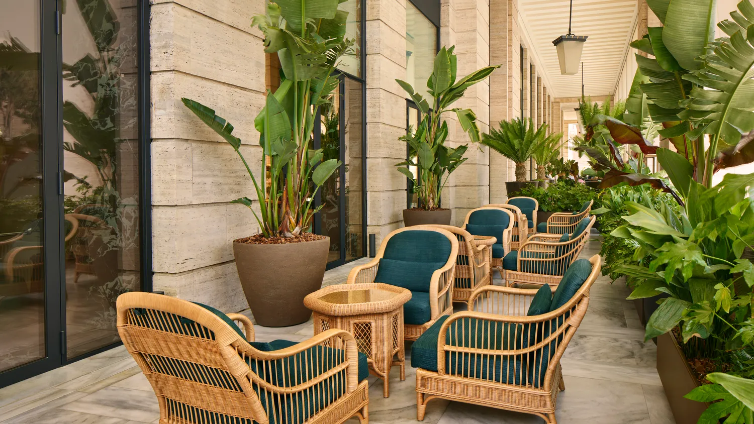 Rattan chairs and tables on a patio at the Bvlgari Hotel Roma, surrounded by lush greenery.
