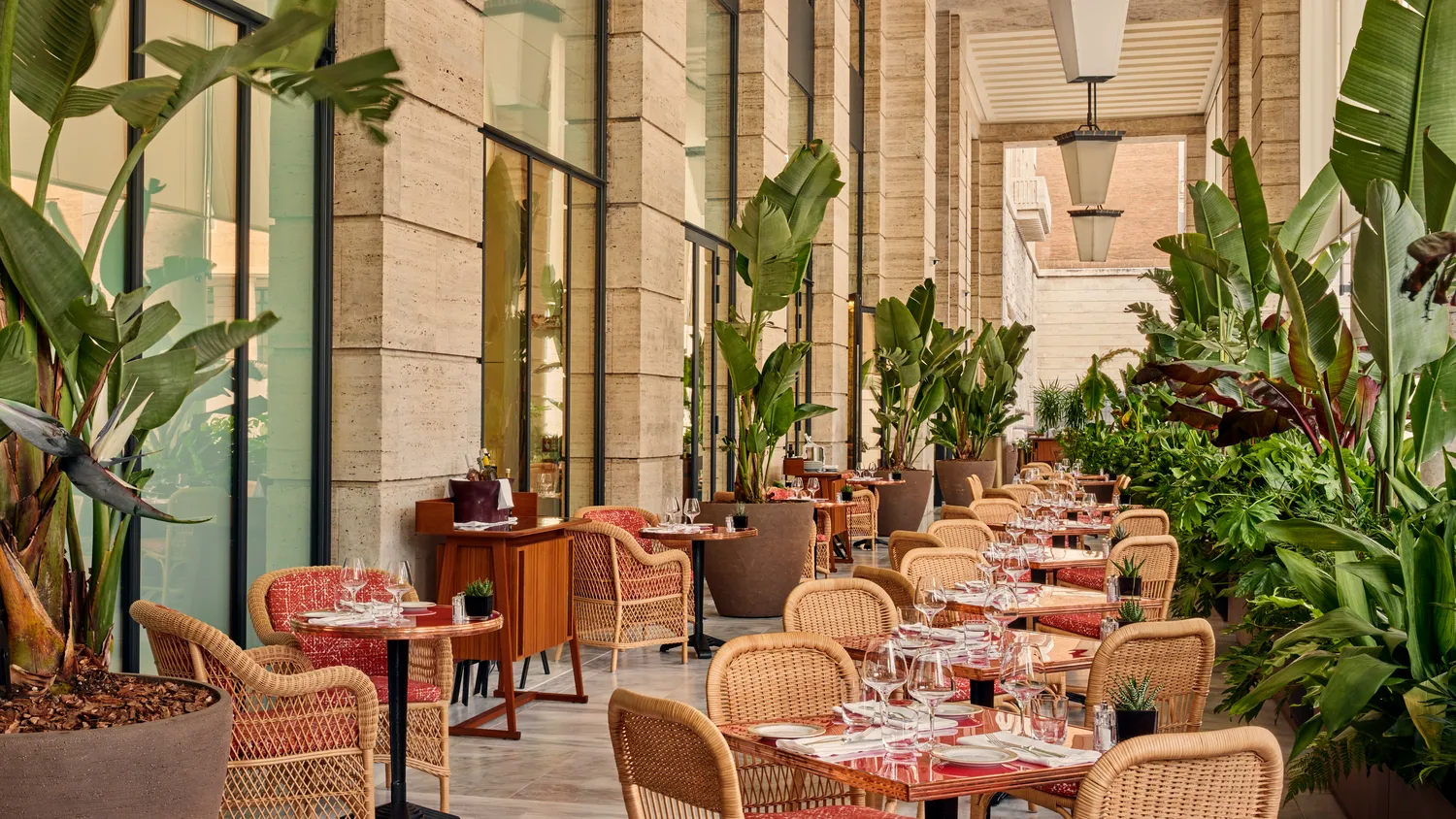 Outdoor patio dining at the Bvlgari Hotel Roma, featuring wicker chairs and lush greenery.