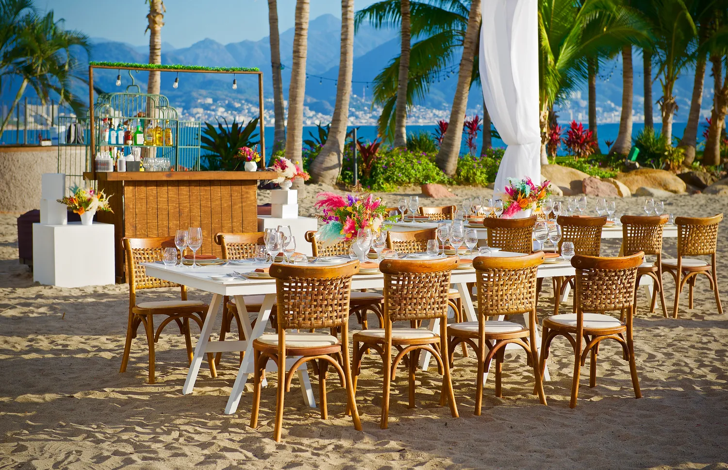 Beach wedding reception at Marriott Puerto Vallarta. Tables with woven chairs are set for a destination wedding.