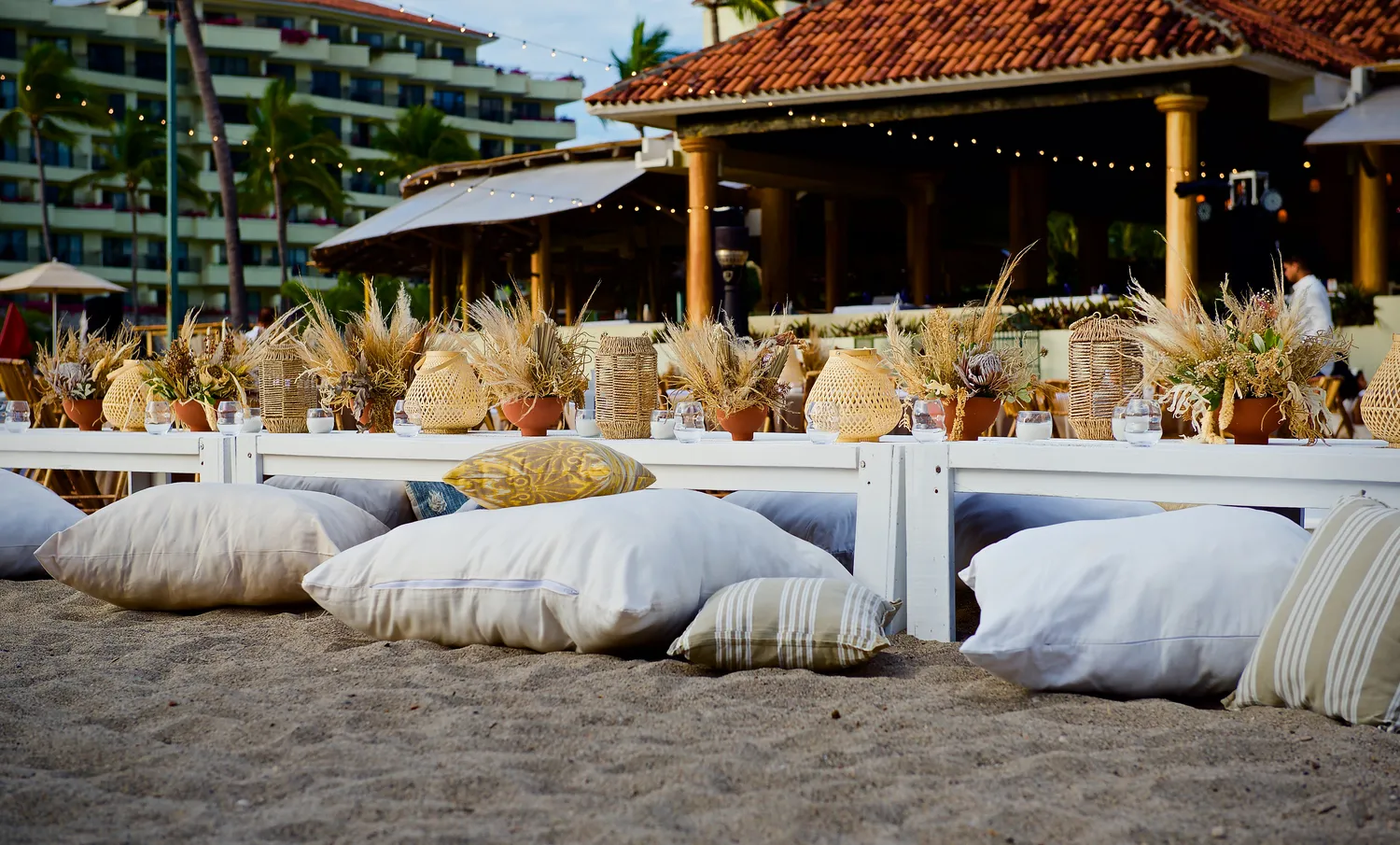 Beach wedding reception at Marriott Puerto Vallarta. Low white tables with pampas grass centerpieces and floor pillows.