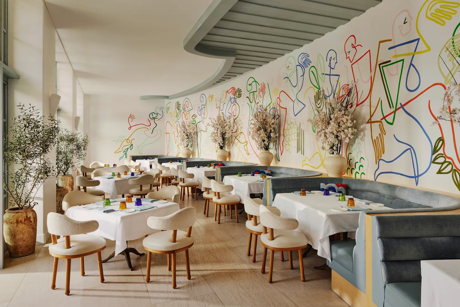 Elegant dining room at the Maybourne Beverly Hills, featuring a curved wall with colorful artwork.