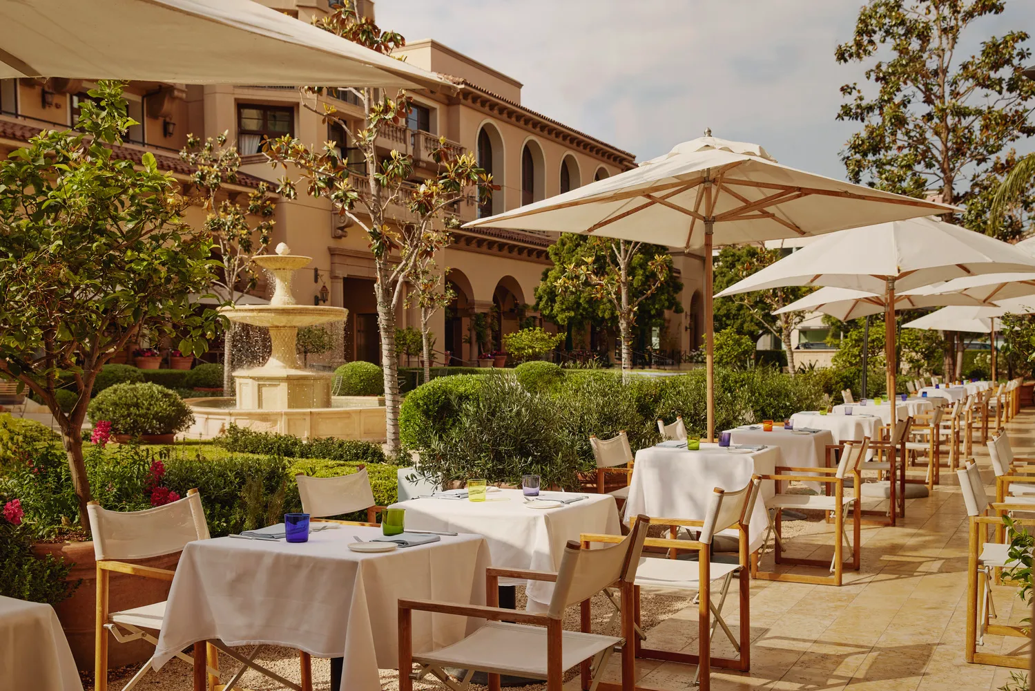 Outdoor patio dining at the Maybourne Beverly Hills, featuring tables set for a meal under umbrellas.