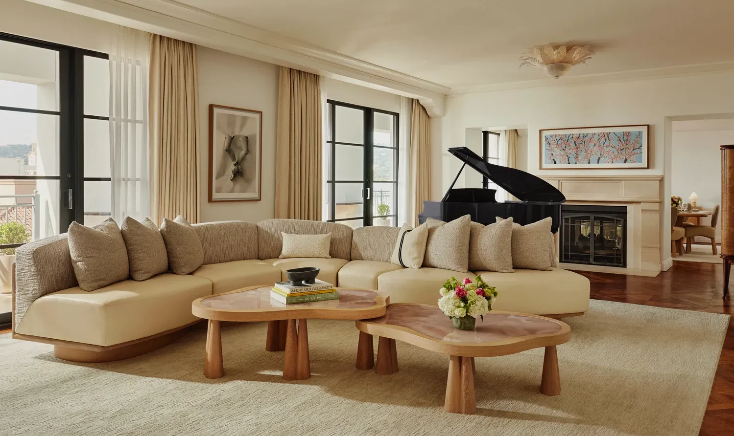 Luxurious living room at the Maybourne Beverly Hills, featuring a curved sofa and grand piano.