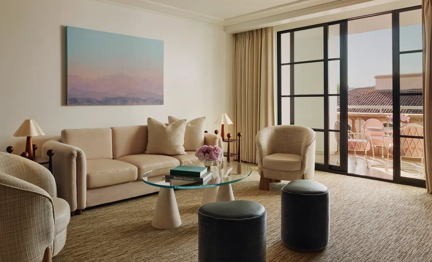 Luxurious living room at the Maybourne Beverly Hills, featuring a beige sofa and chairs, and a view of a private balcony.