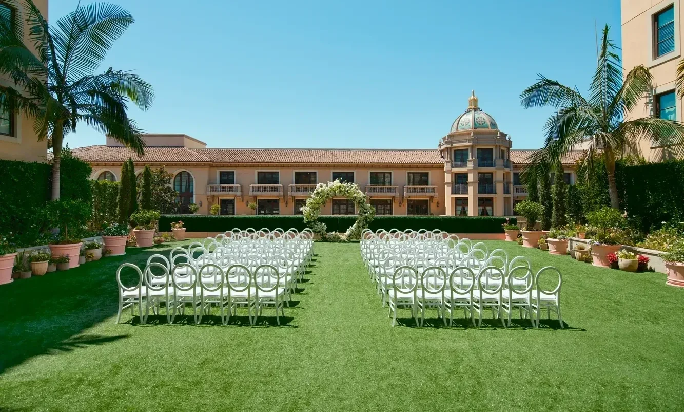 Outdoor wedding ceremony setup at the Maybourne Beverly Hills, featuring white chairs and a floral arch.