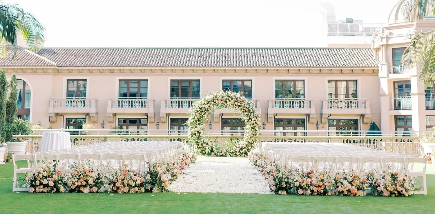 Elegant outdoor wedding ceremony setup at the Maybourne Beverly Hills, featuring a floral arch and rows of white chairs.