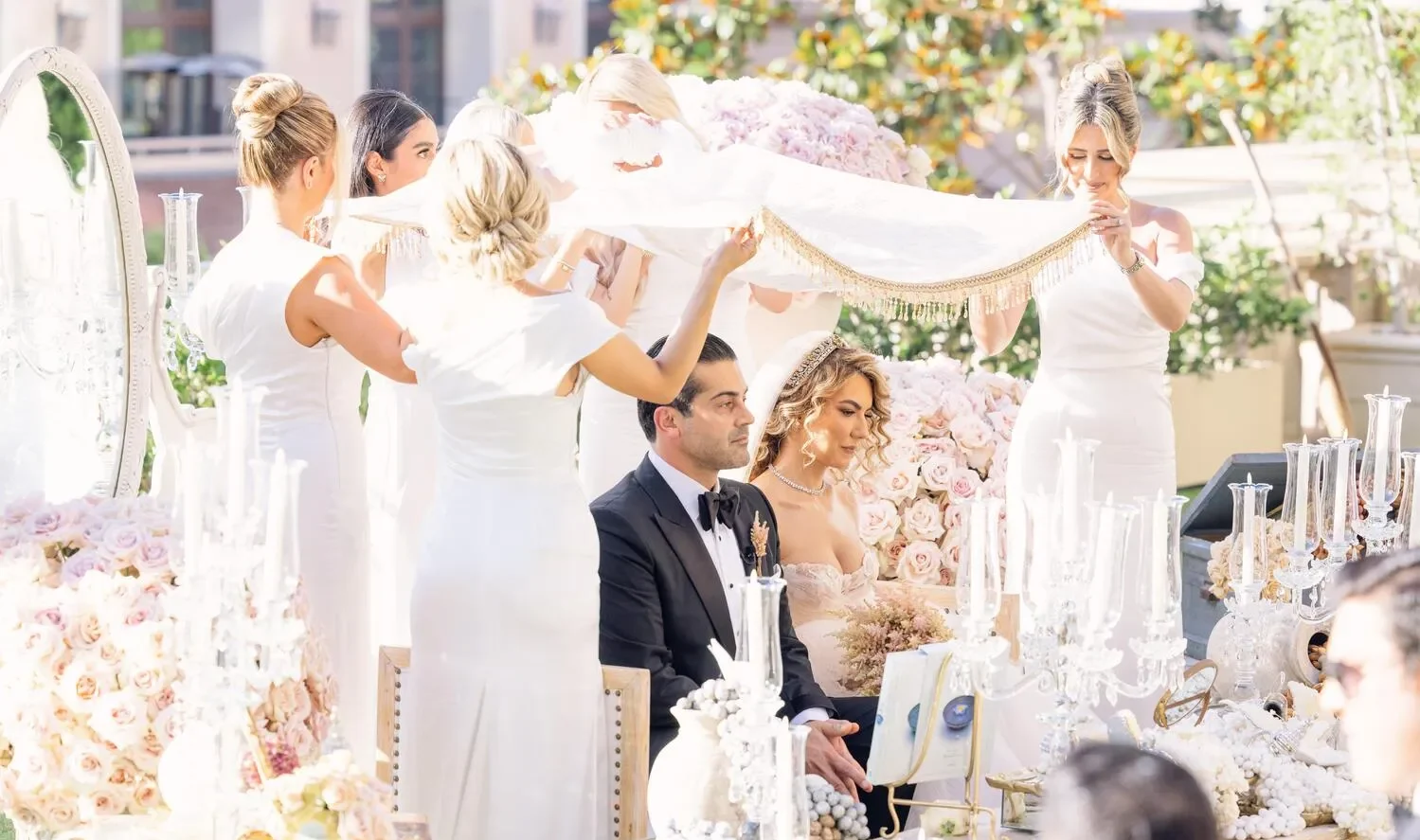 Bride and groom at a luxurious Beverly Hills wedding ceremony, with bridesmaids holding a veil overhead.