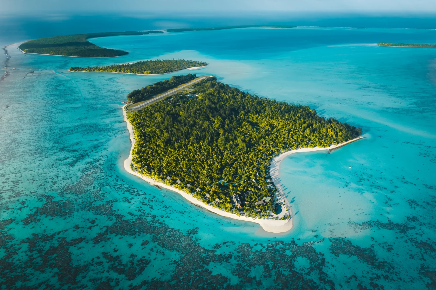 Aerial view of a tropical island with a runway, lush vegetation, and pristine beaches.