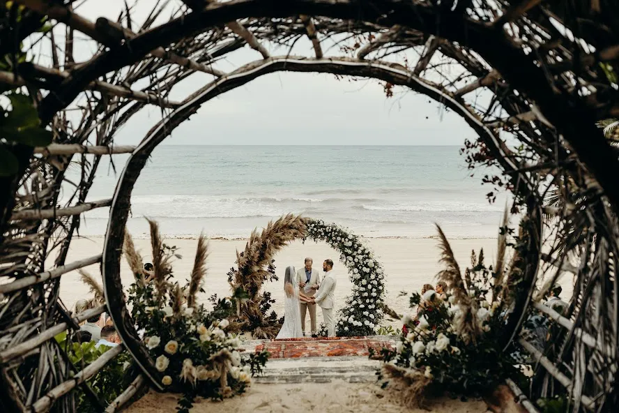 Beach wedding ceremony at Casa Malca Tulum, a luxury wedding venue. Bride and groom exchange vows under floral arch.
