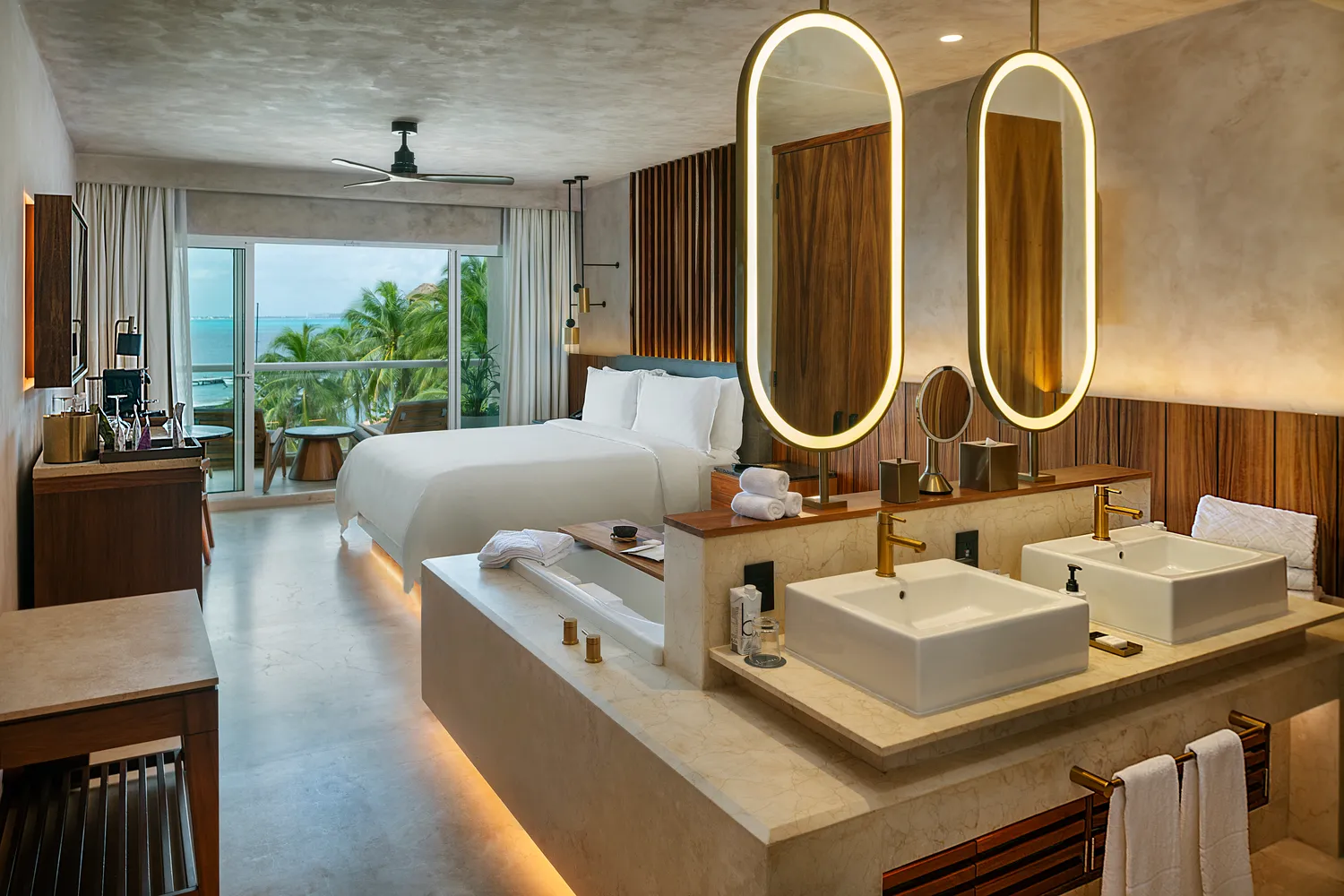 Luxury suite at Almare Isla Mujeres with ocean view, king bed, and modern bathroom featuring a soaking tub and double vanities.