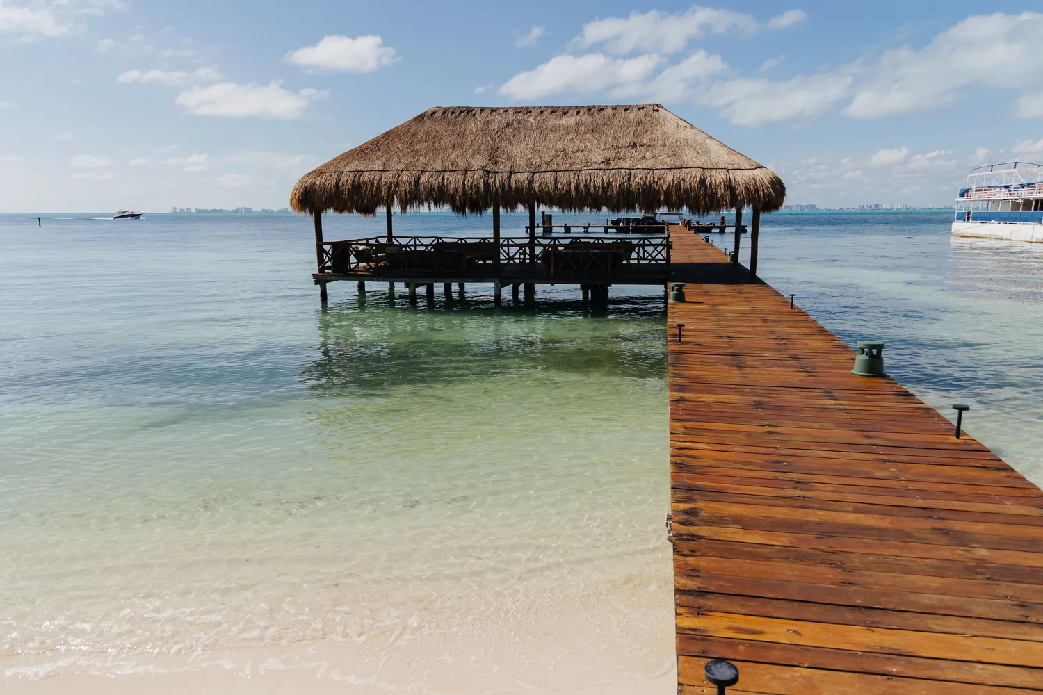 Wooden pier leading to a thatched-roof palapa overwater at Almare Isla Mujeres.