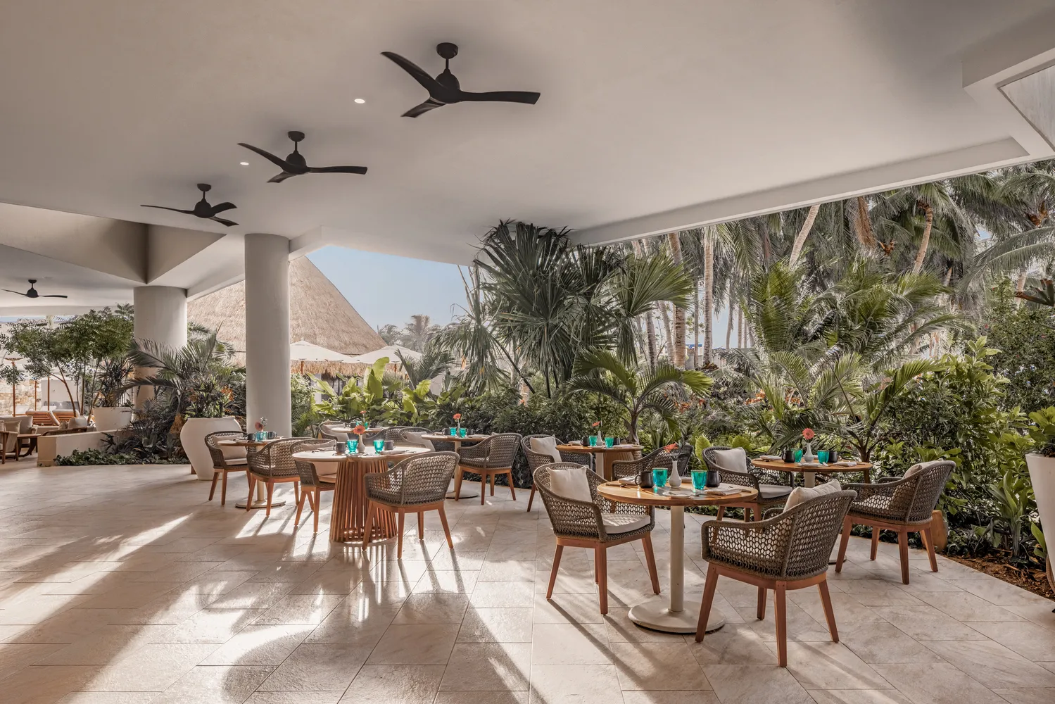 Outdoor patio dining at Almare Isla Mujeres, featuring elegant tables and chairs amidst lush tropical landscaping.