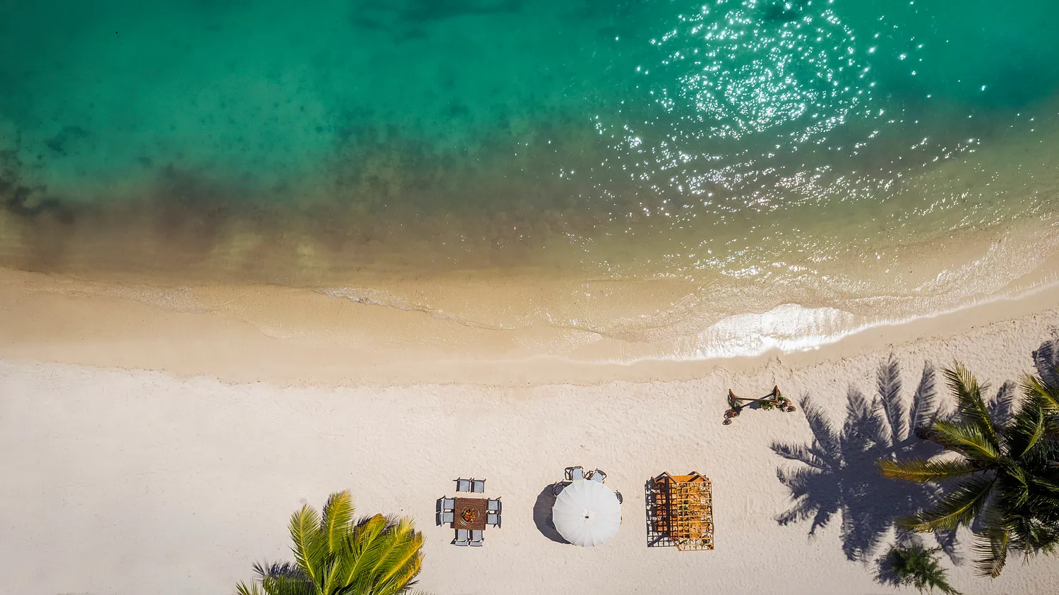 Aerial view of Almare Isla Mujeres beach wedding setup: tables, umbrella, and ceremony arch.