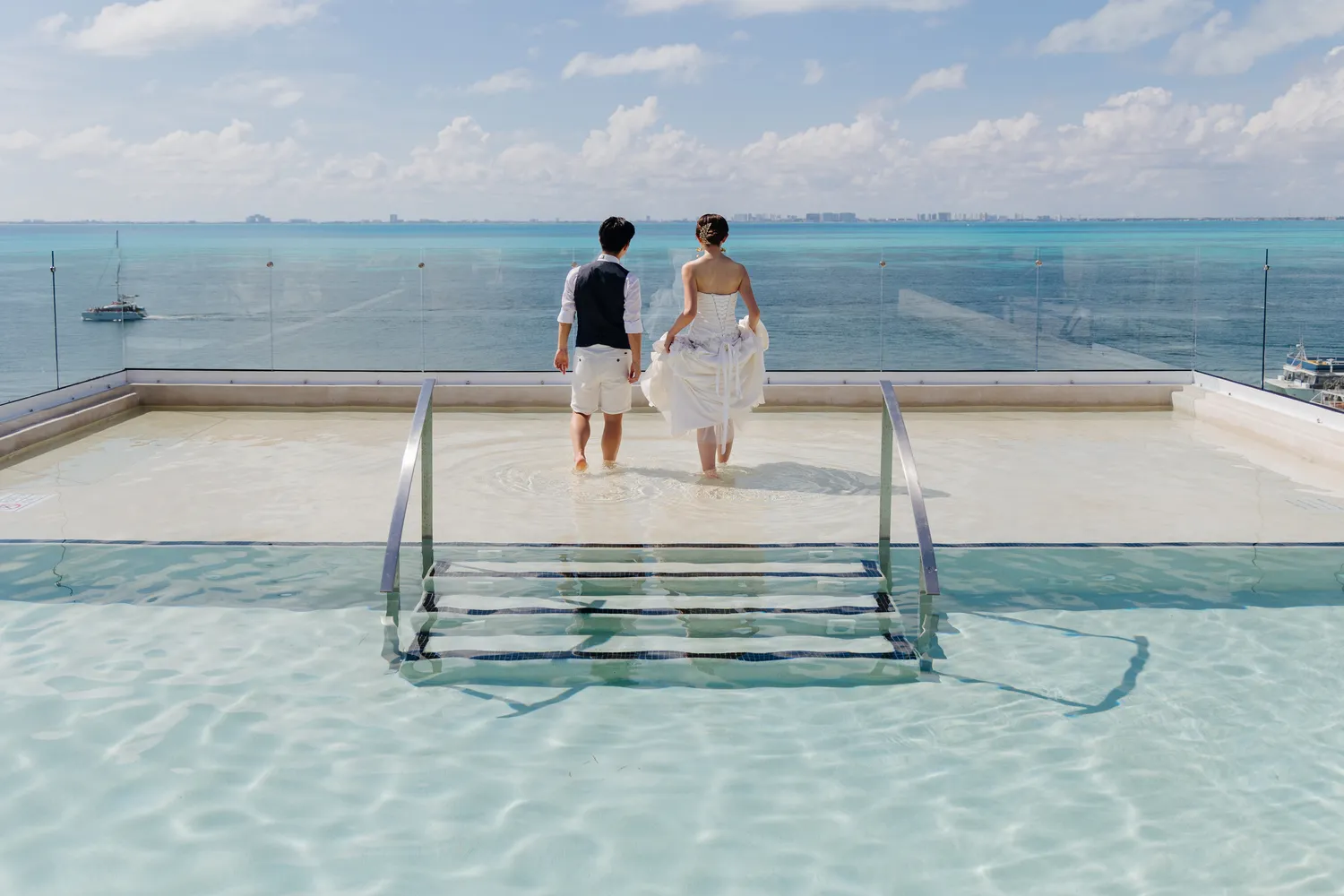 Bride and groom walking barefoot in shallow water at Almare Isla Mujeres, a luxury resort.