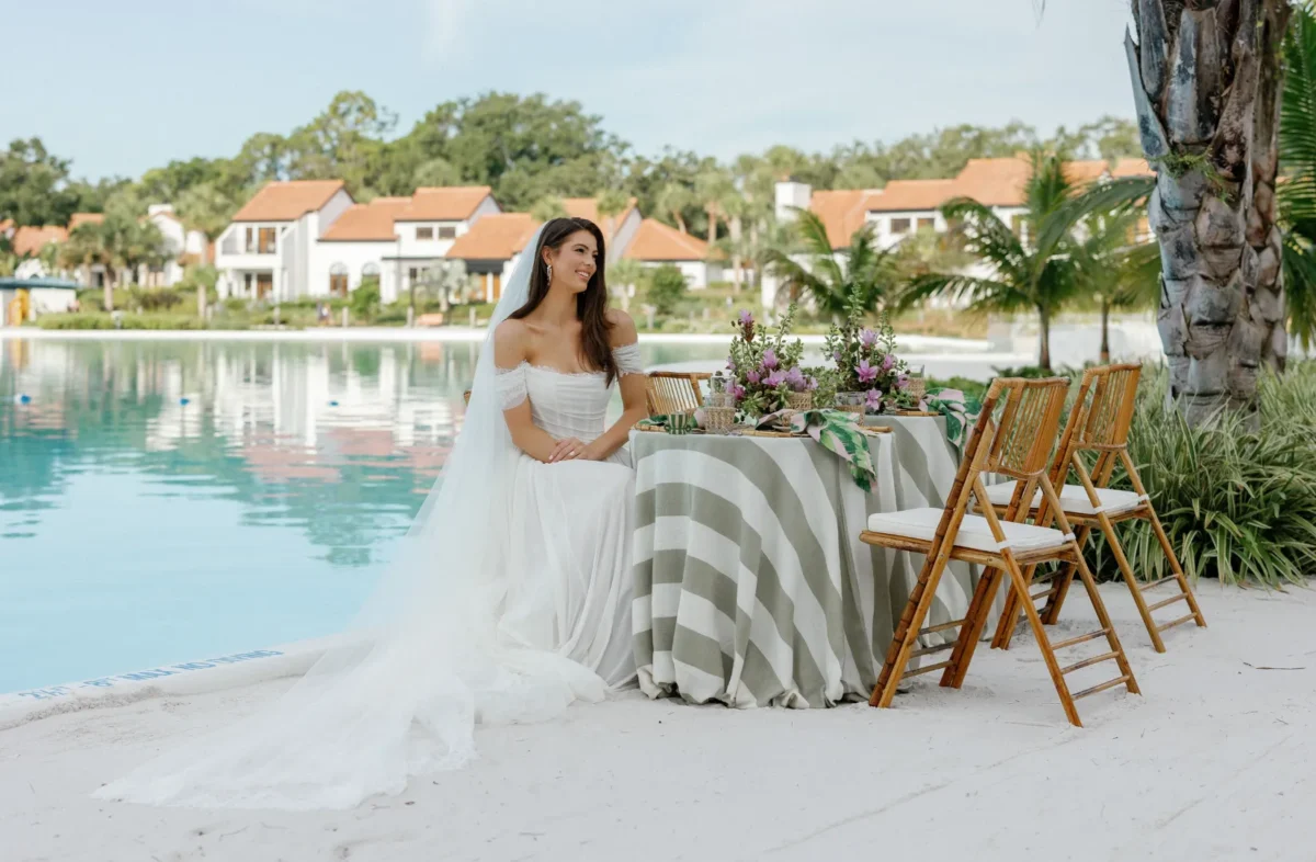 Bride in wedding dress sits at a table by a pool at the Conrad Orlando.