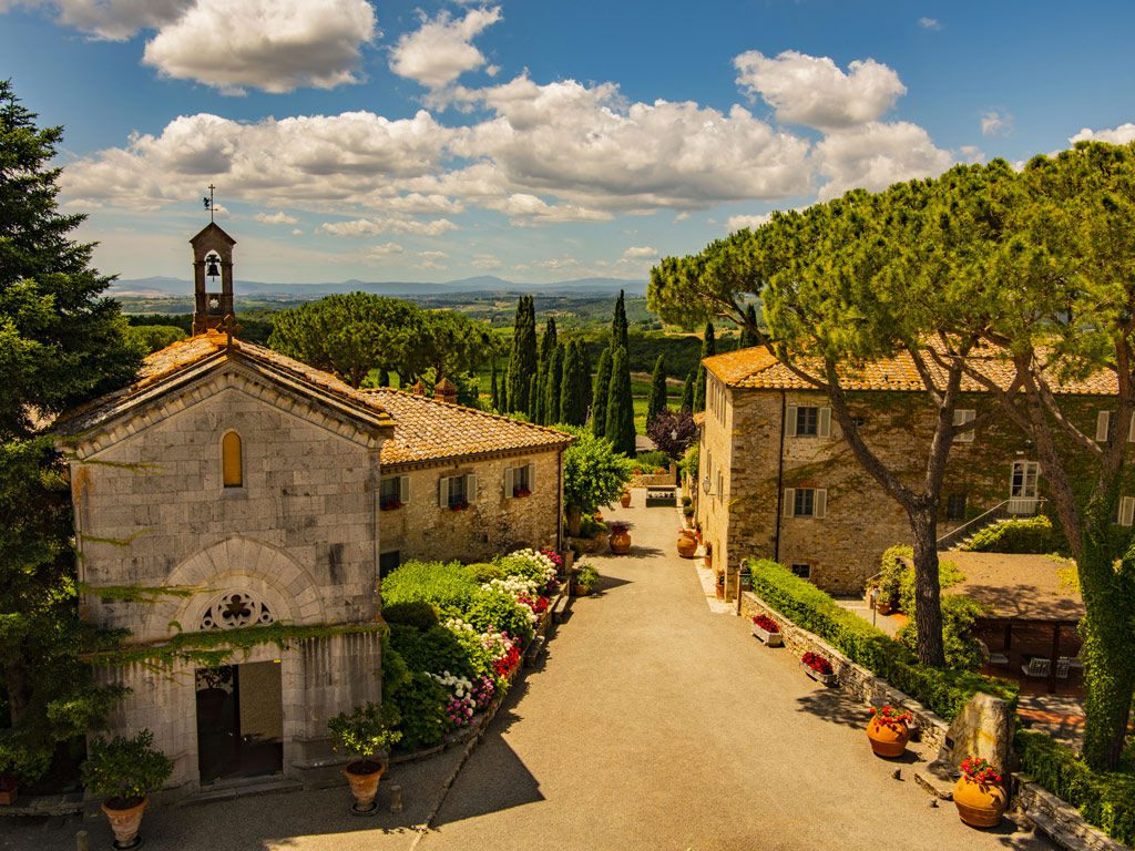Tuscan borgo with stone buildings and a bell tower under a blue sky with clouds. Property descriptions meaning.