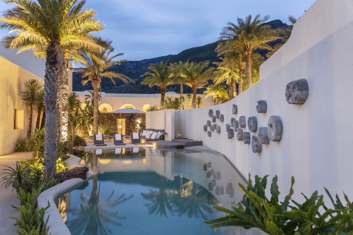 Luxury resort pool at dusk, palm trees reflected in water.