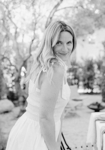 Woman in a white dress smiling outdoors in a sunlit garden